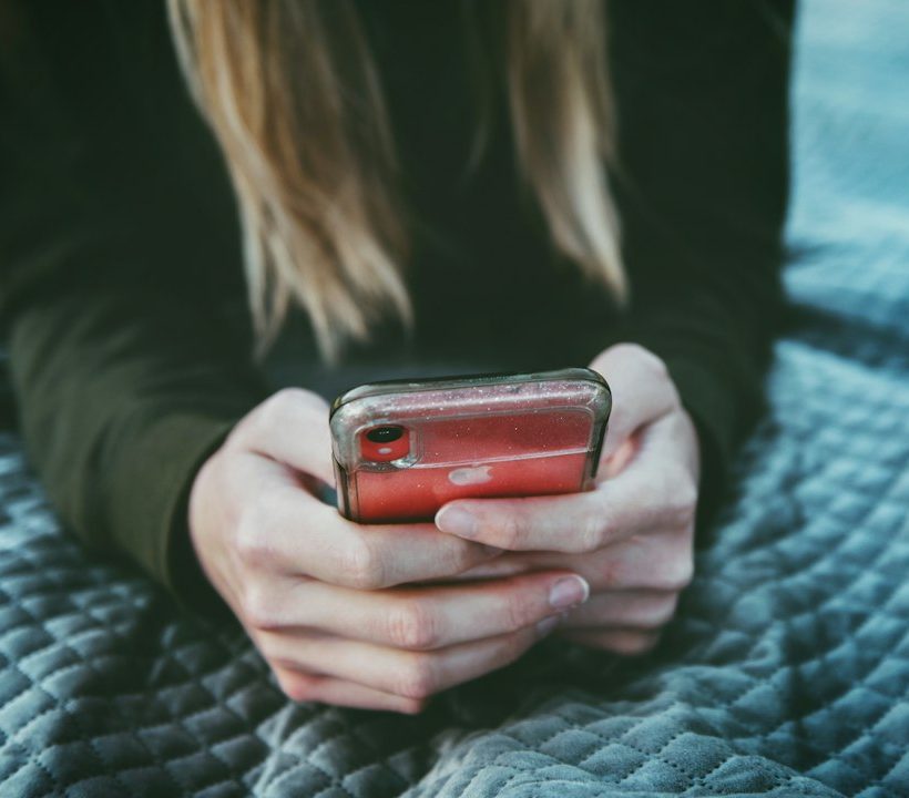 Egy kamasz kezében telefon, az ágyon fekve, arca nem látszik.