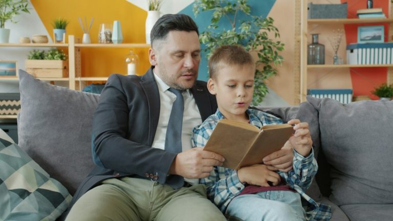Apa és kisfia a kanapén ülve együtt olvas egy könyvet.